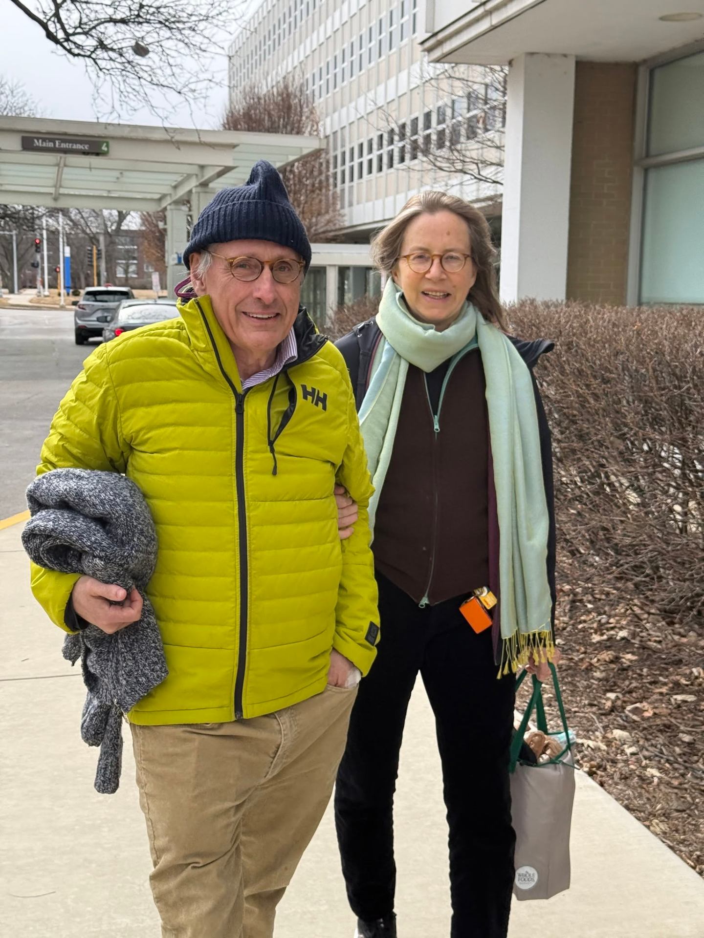 Pierre and his wife walking arm-in-arm outside a hospital entrance.